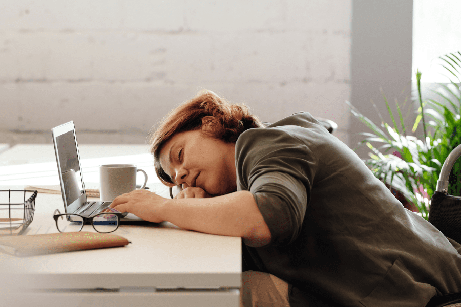 tired mom sleeps at computer desk in front of coffee